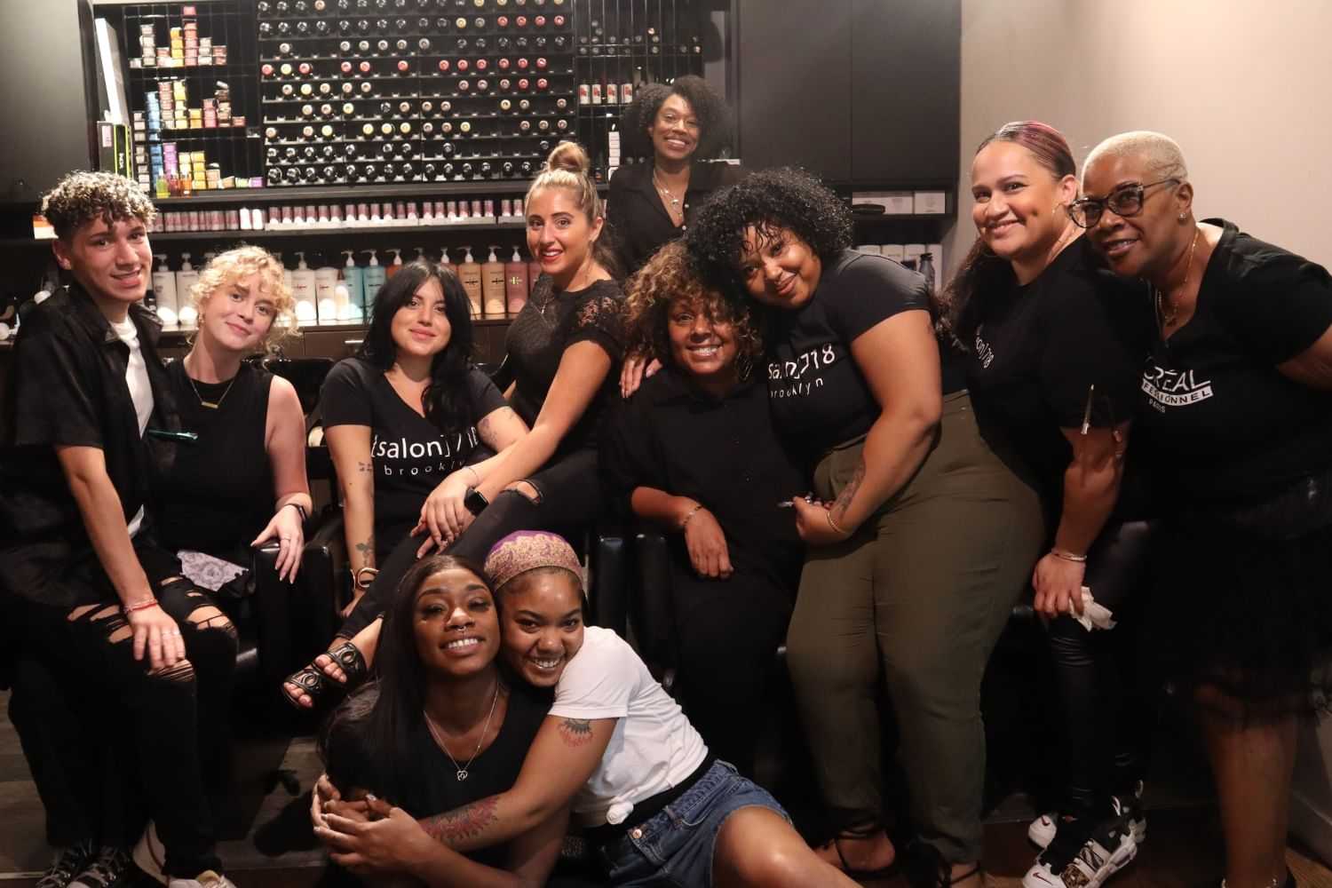 Group of smiling salon staff posing in front of hair product shelves.