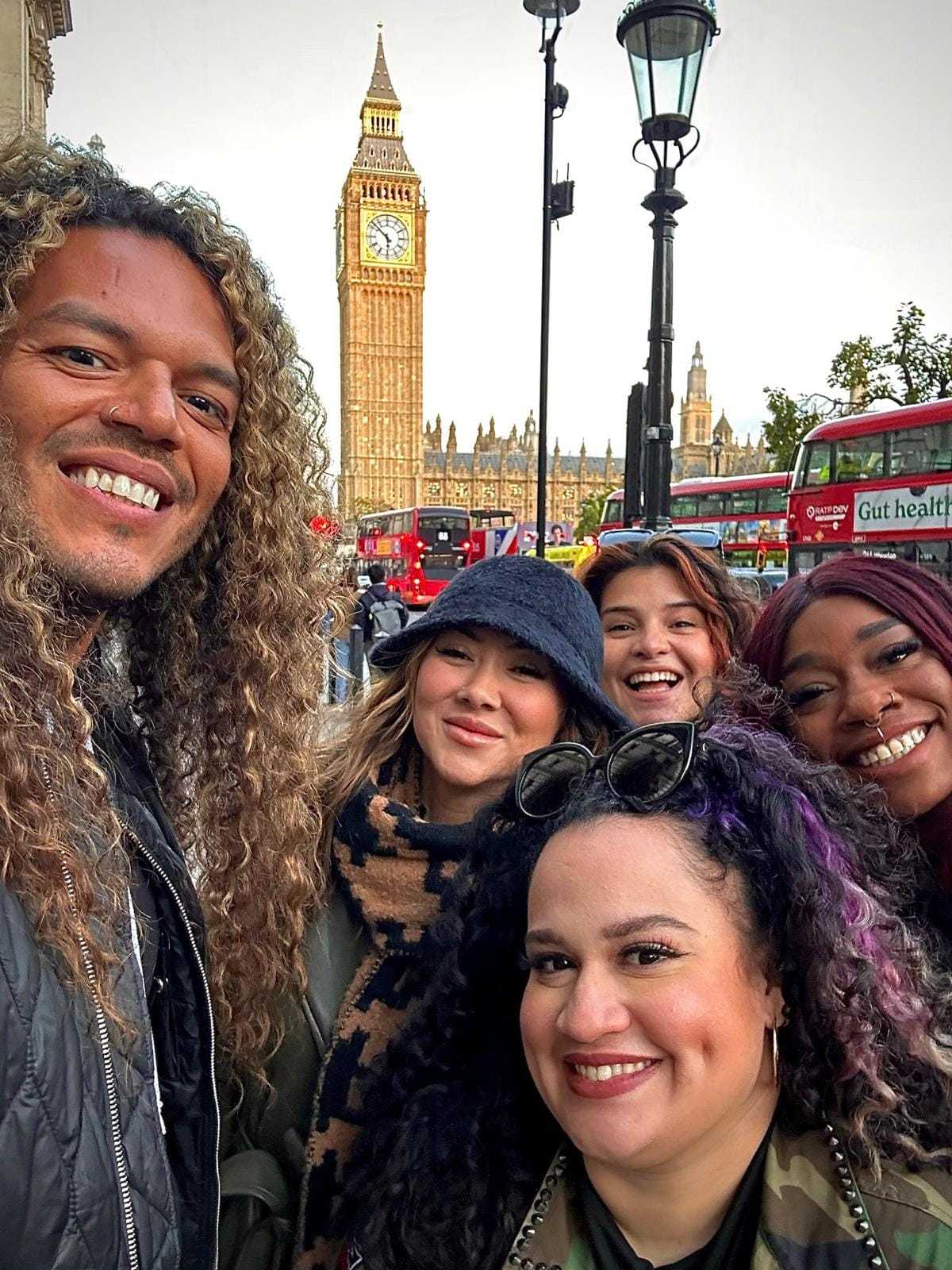 Group of friends smiling, posing in front of Big Ben and London buses.