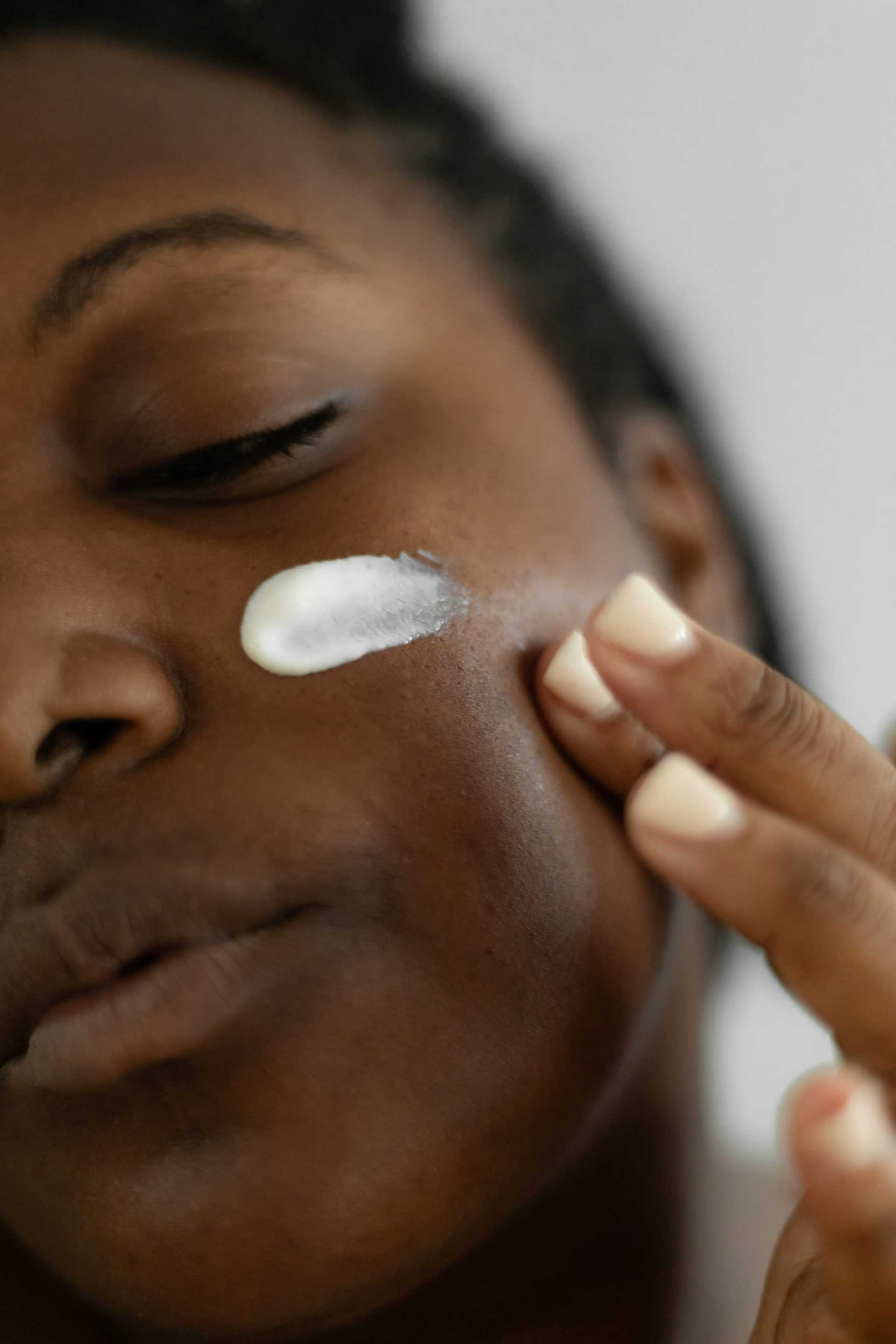 Person applying skincare cream to their cheek with fingers.
