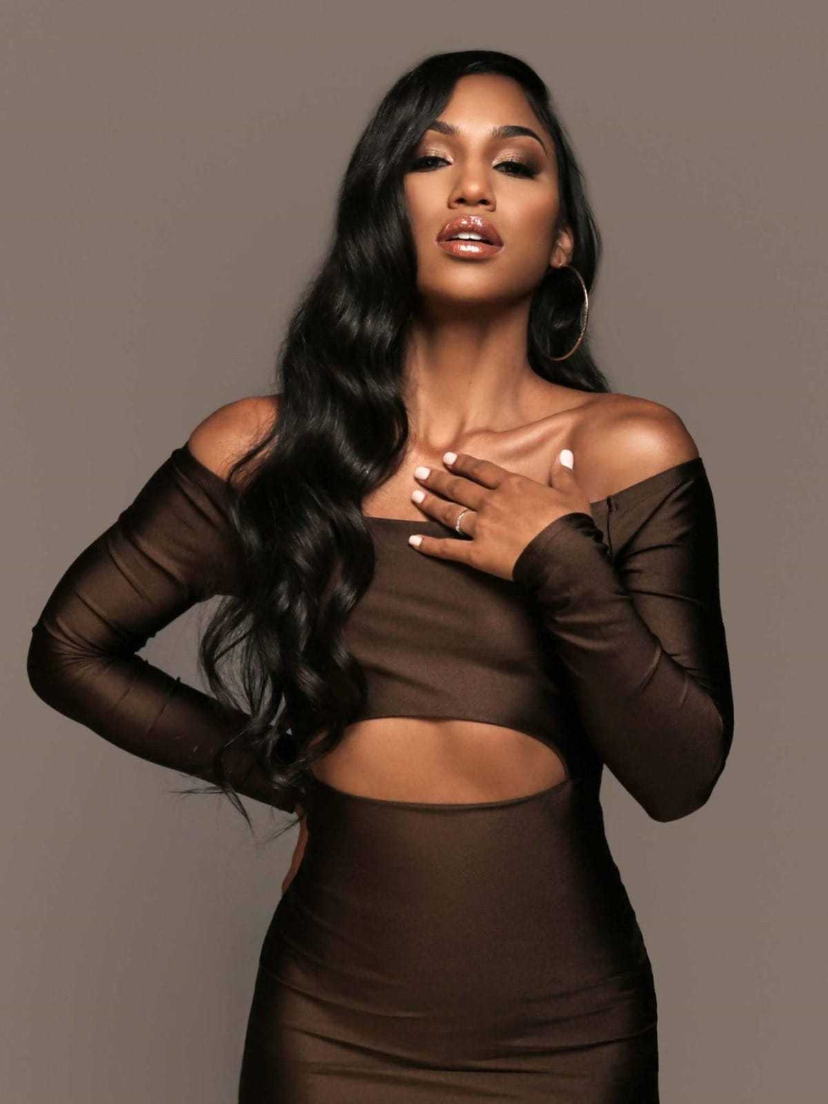 Woman in a brown dress poses with confidence on a neutral background.