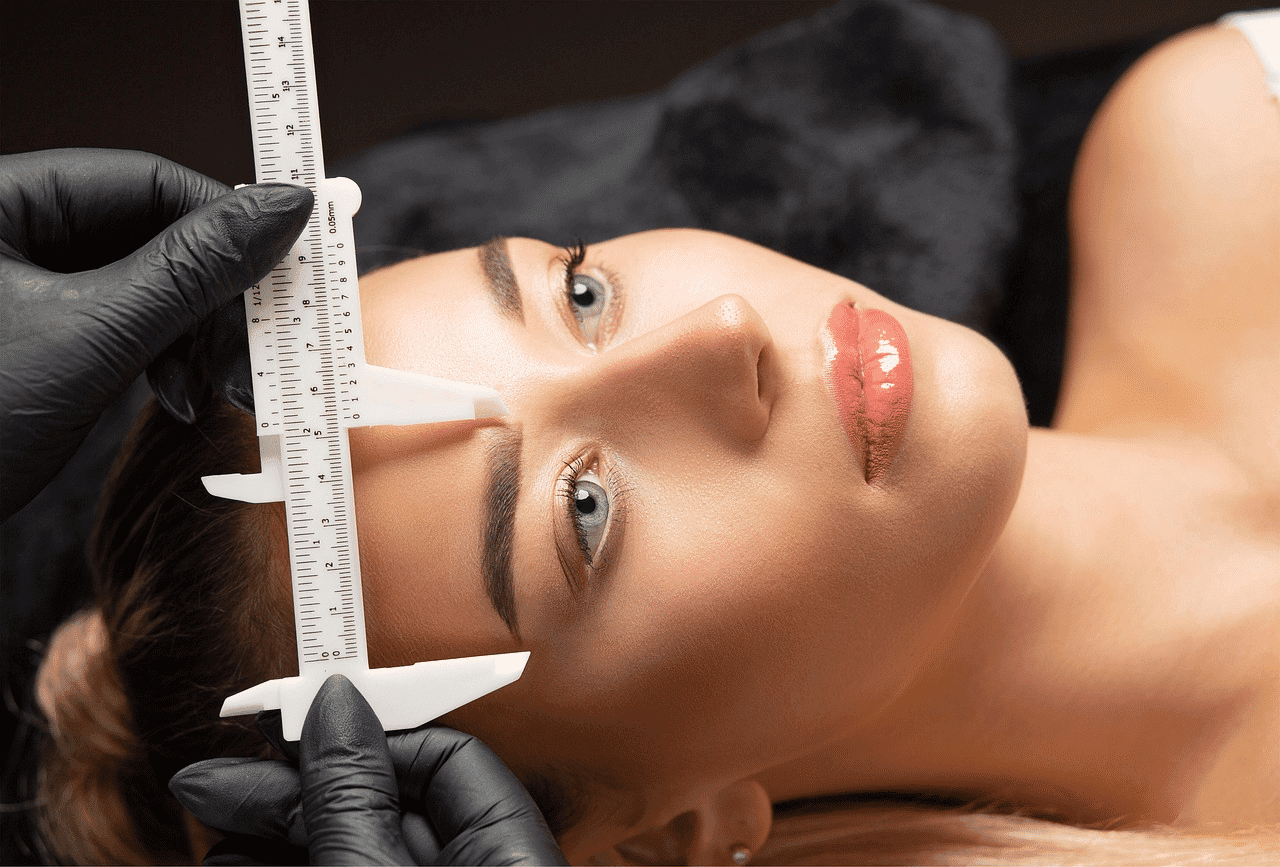 Cosmetic procedure: Gloved hands measuring woman's forehead with calipers.
