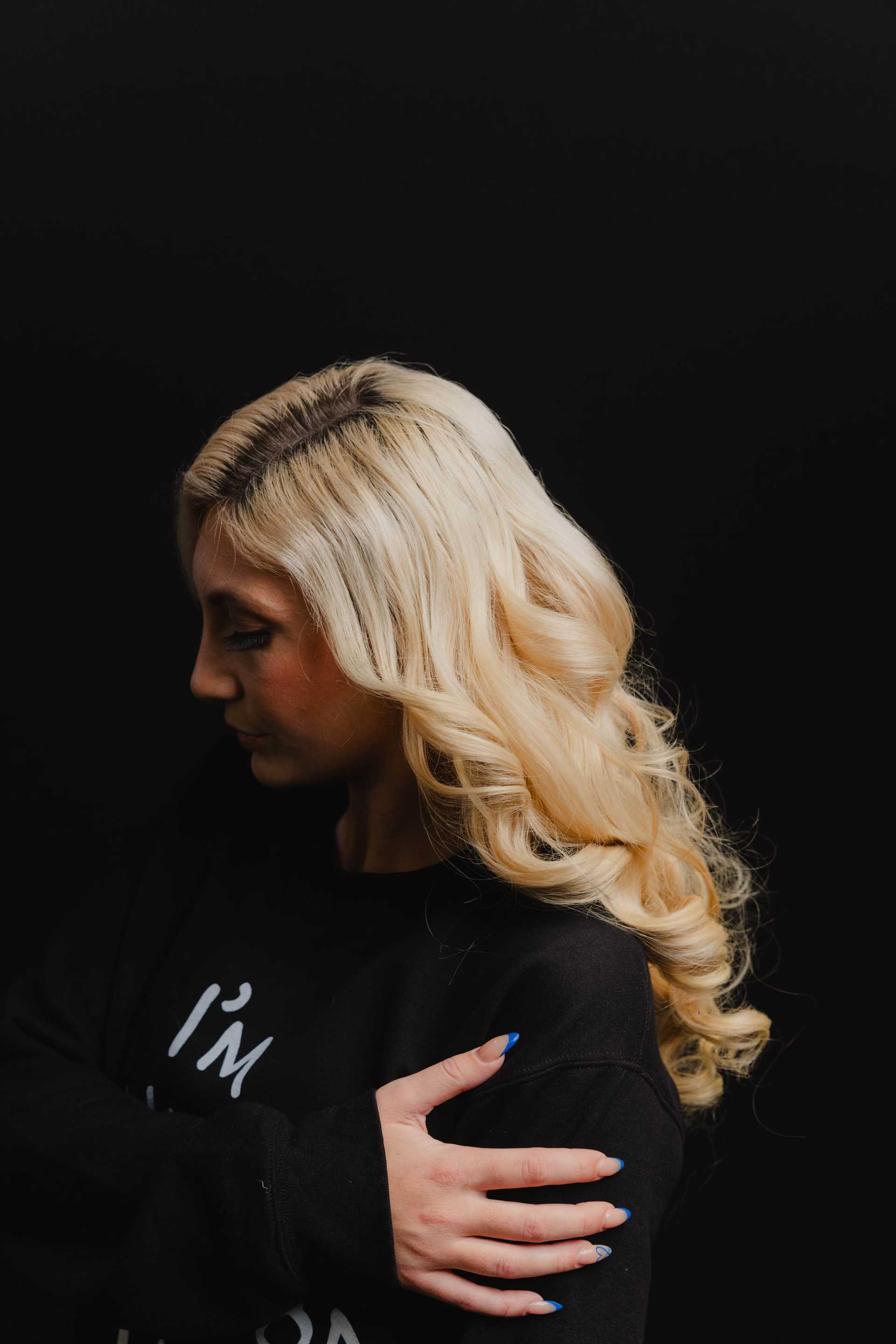 Blonde woman in black sweater with curled hair against a dark background.