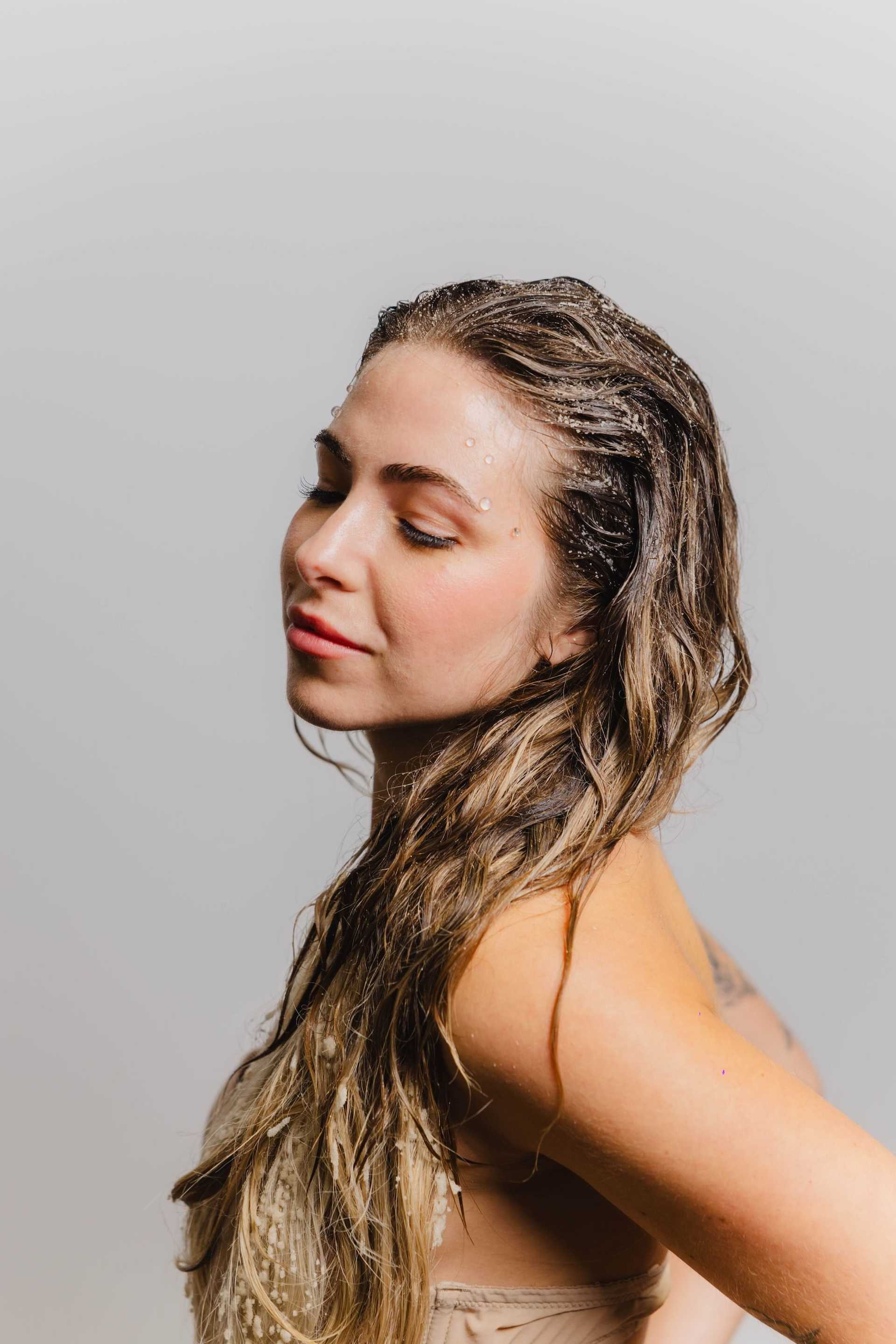 Young woman with wet hair, eyes closed, in a relaxed pose against a plain background.