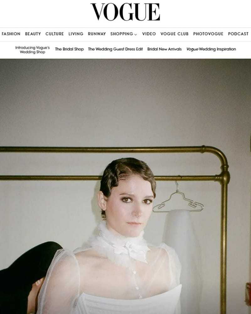 Woman in elegant white dress with wavy hair, standing in a softly lit room.