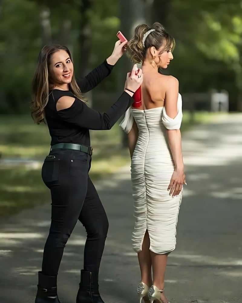 Woman in white dress getting hair styled outdoors by hairstylist with hairspray.